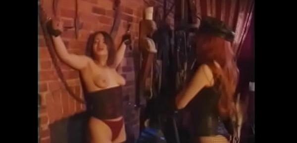 Red-haired mistress in a leather cap humiliates her slave and spanks her with a whip on an appetizing ass